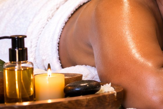 Warm massage oil, candle and a smooth black stone on a wooden tray